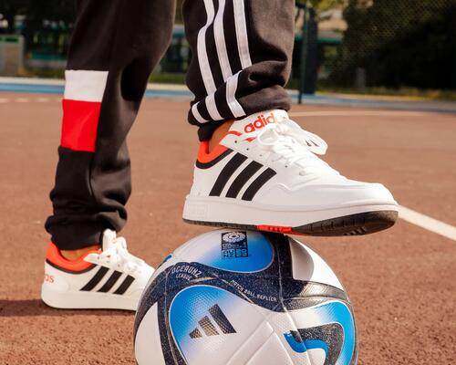 osoba w butach i spodniach firmy adidas trzymająca nogę na piłce do piłki nożnej