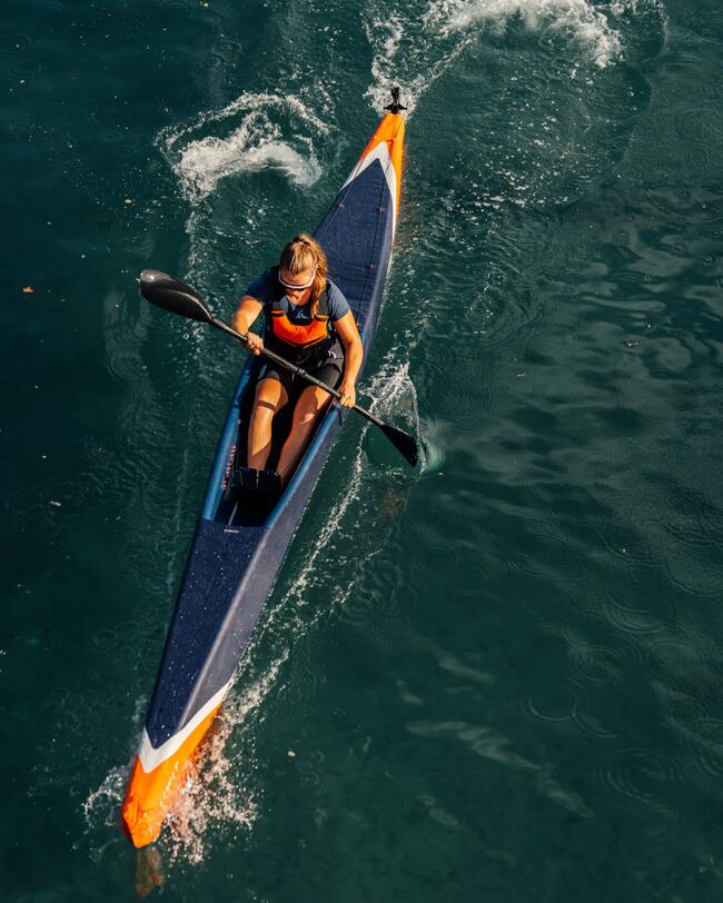 Paddlerin im farbenfrohen Kajak auf türkisblauem Wasser, spritzende Gischt, dynamische Bewegung.