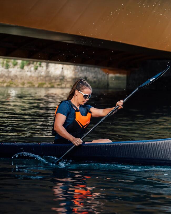 Frau fährt im Kanu übers Wasser. Sie trägt eine Sonnenbrille.