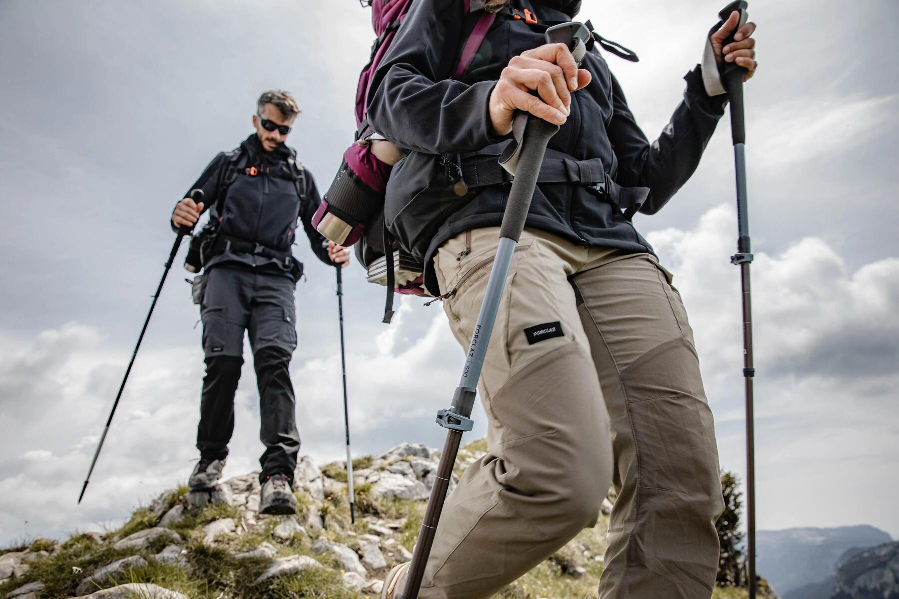osoby wędrujące po górach  z plecakami turystycznymi na plecach trzymając za rękojeść kijki trekkingowe