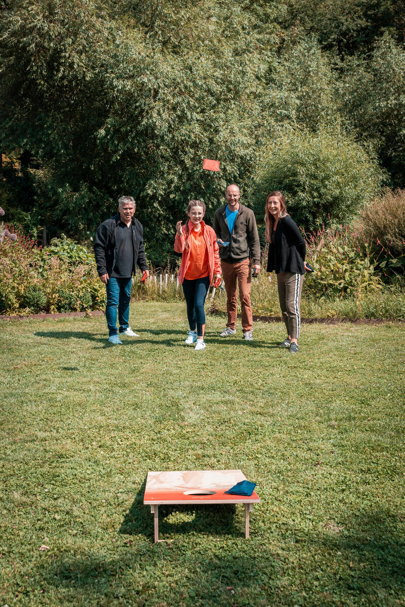 Četvoro odraslih igra Cornhole u sunčanom dvorištu.