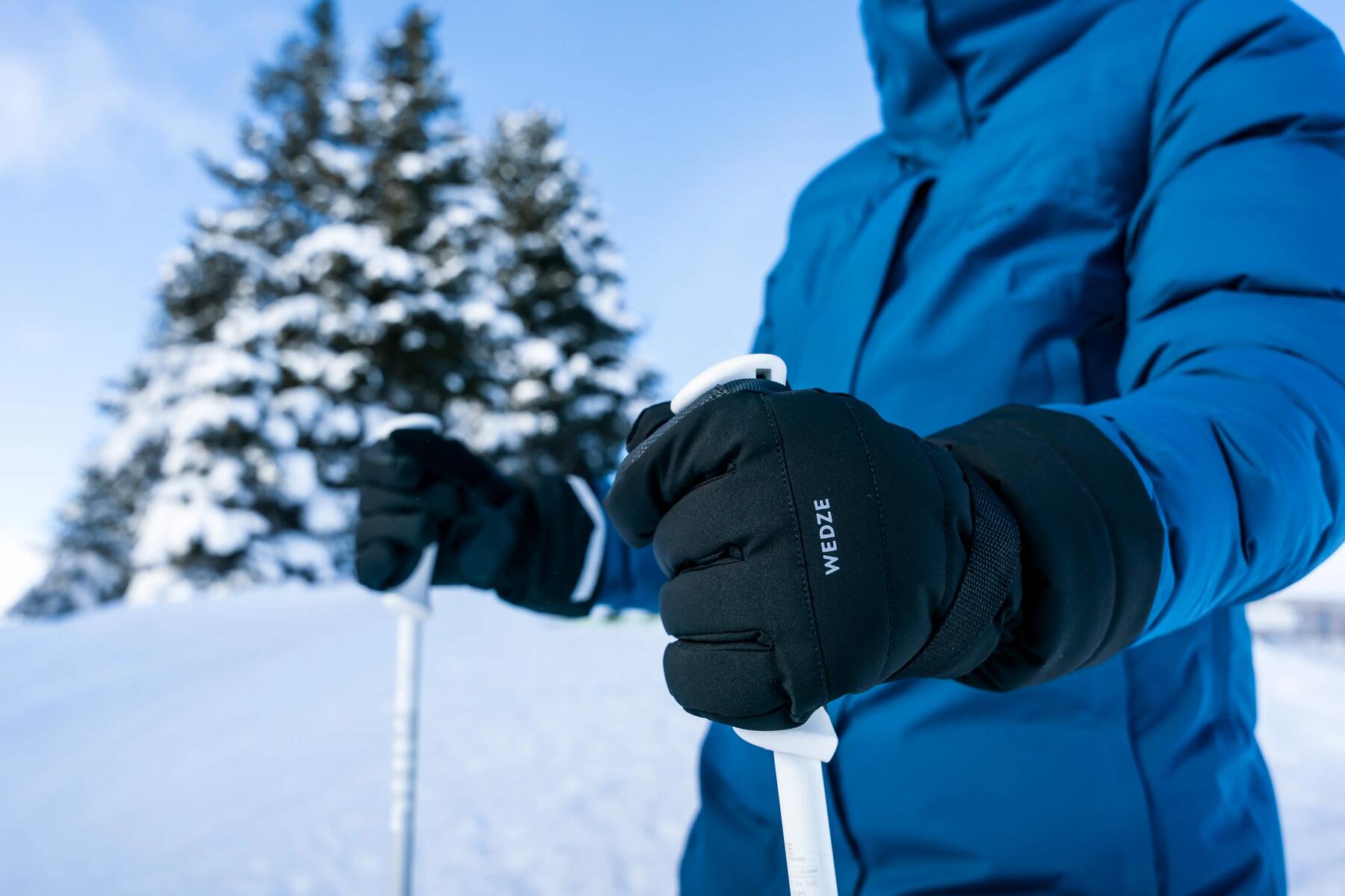 Mężczyzna ubrany w kurtkę narciarską w rękawicach trzymający kijki narciarskie
