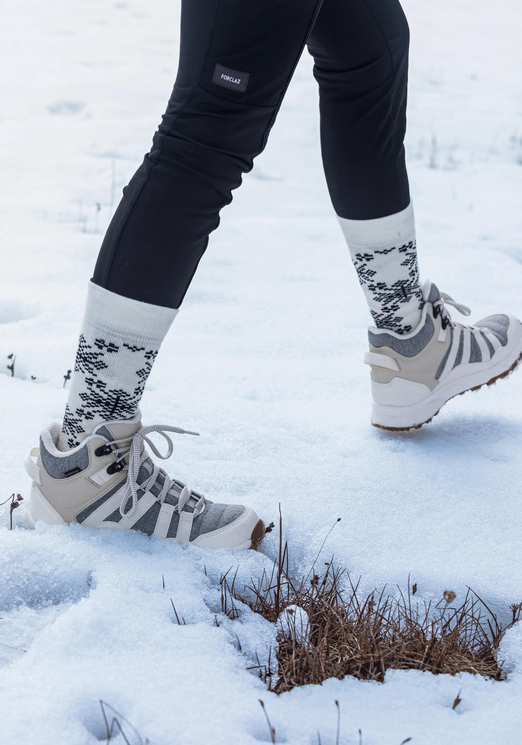 Persoon met wandelsokken en schoenen die wandelt in de sneeuw. Je ziet alleen de benen van de persoon.