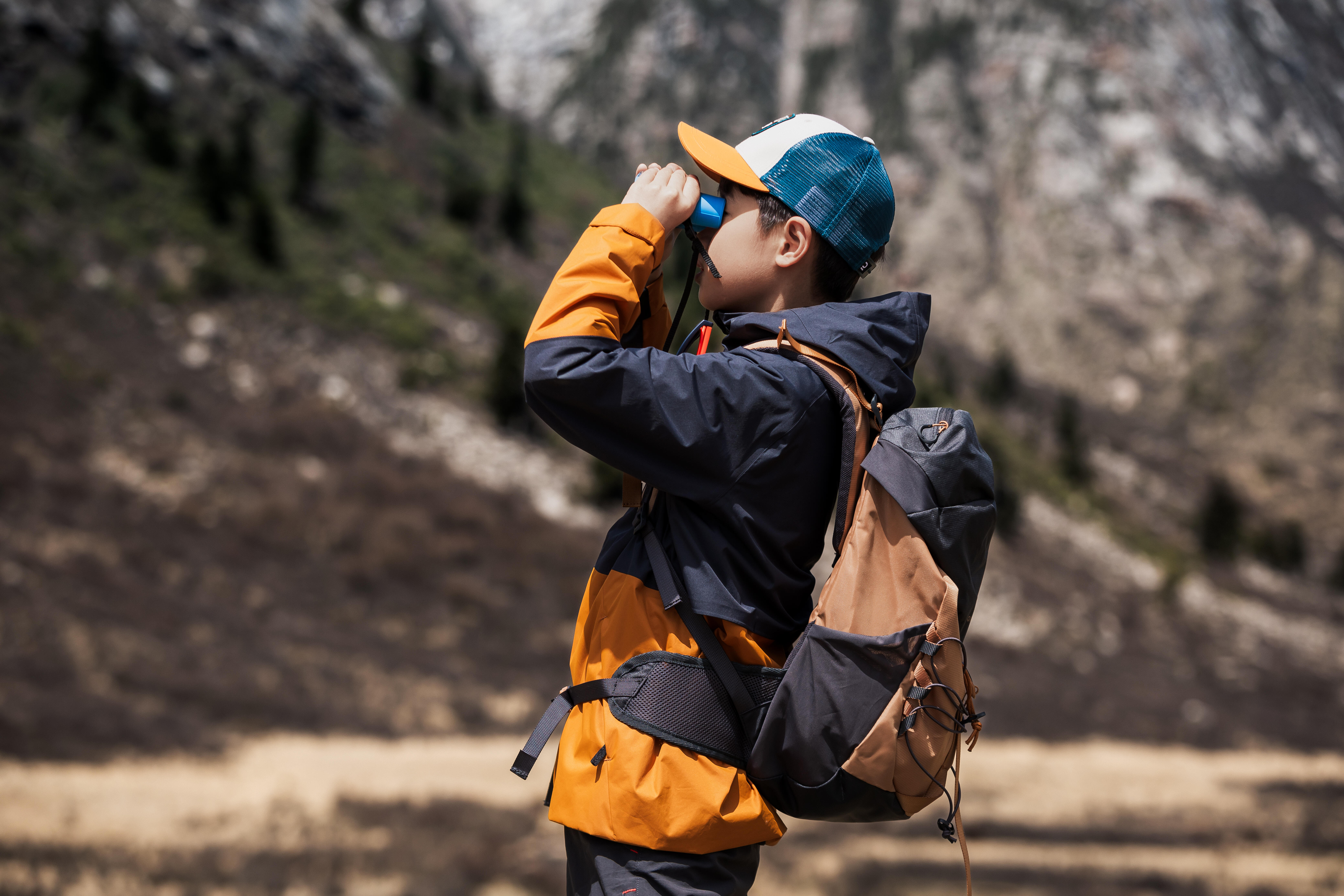 Child hiking with backpack while using binoculars outdoors