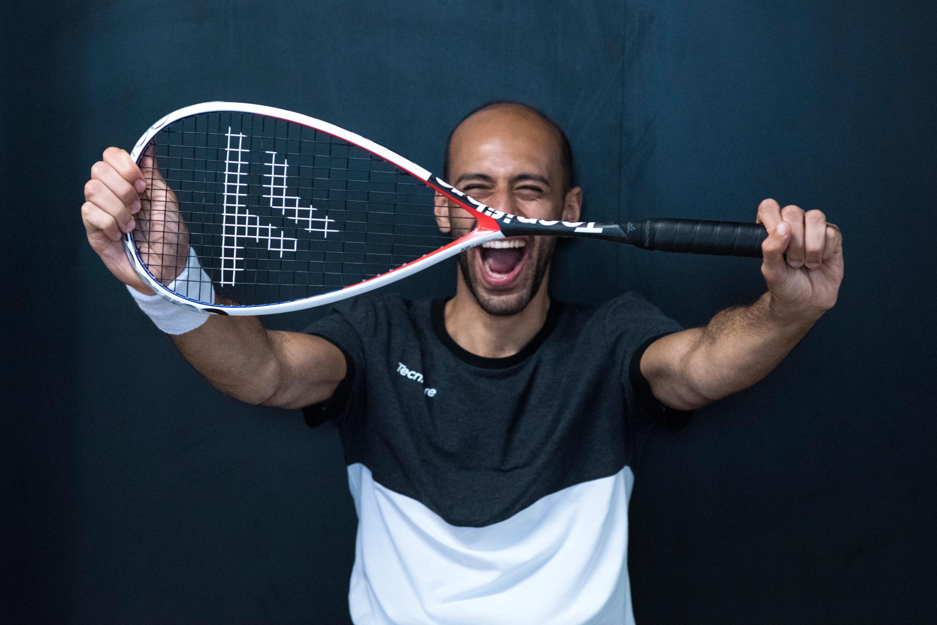 Ein Mann hält einen Squash-Schläger vor sein Gesicht, der Schläger hat einen weißen Rand und schwarze Saiten mit einem Logo.