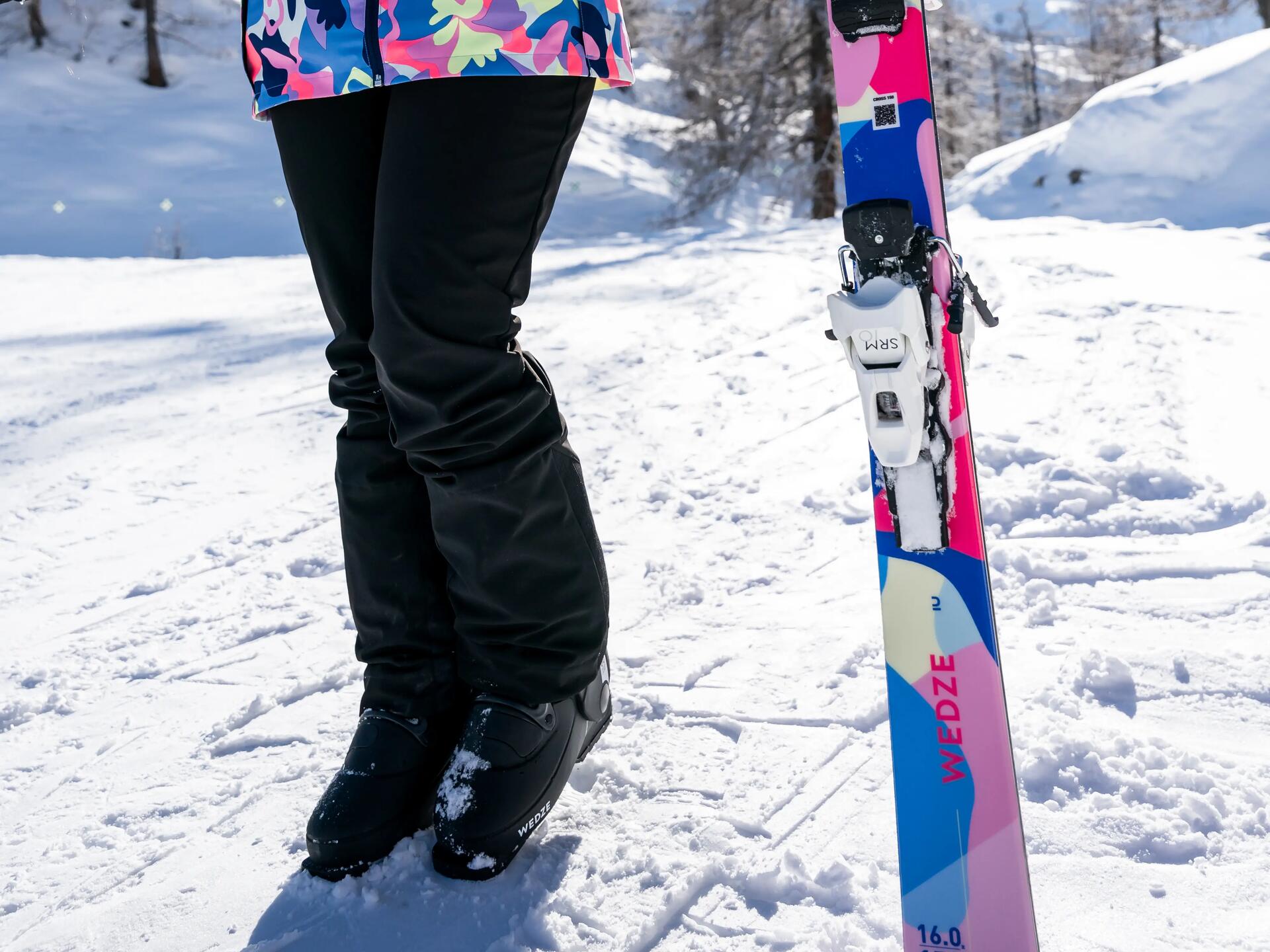 kobieta stojąca na śniegu w stroju i butach narciarskich trzymając w ręce narty
