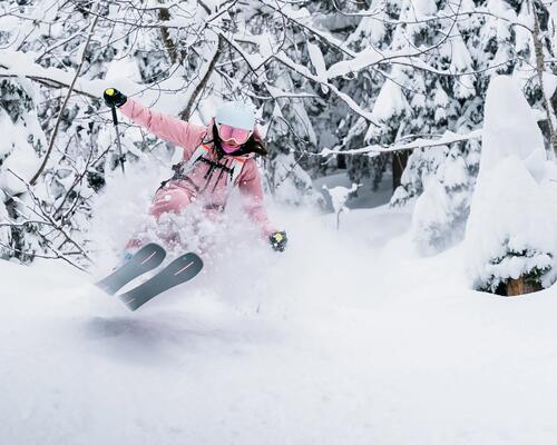 kobieta w kasku i goglach narciarskich jadąca na nartach z kijkami narciarskimi w rękach
