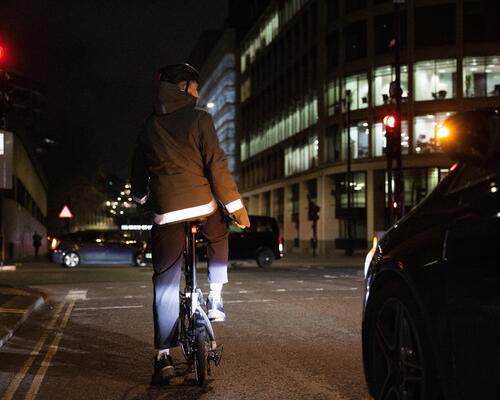 a cyclist riding in front of a carvat night wearing a Men's City Cycling Night Visibility Rain Jacket 