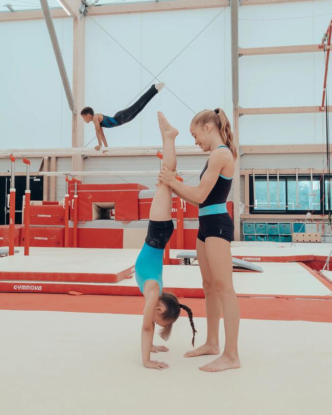 Ein Junge turnt auf einem Stufenbarren. Zwei Mädchen üben einen Handstand.