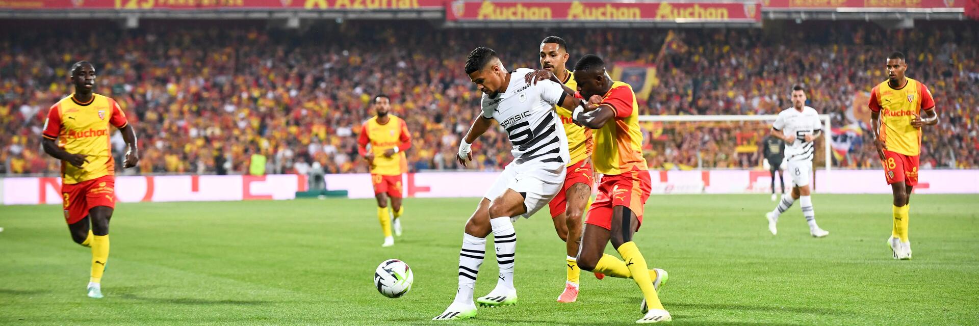 Spieler vom RC Lens und Stade Rennes kämpfen im vollen Stadion um den Ball.