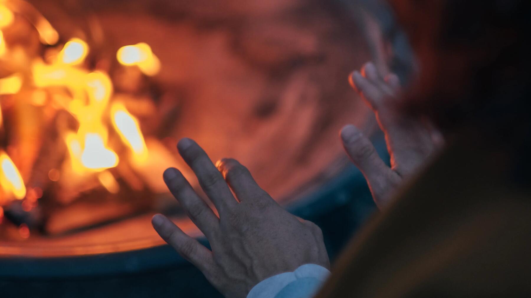 Osoba ogrzewająca ręce przy rozpalonym ognisku