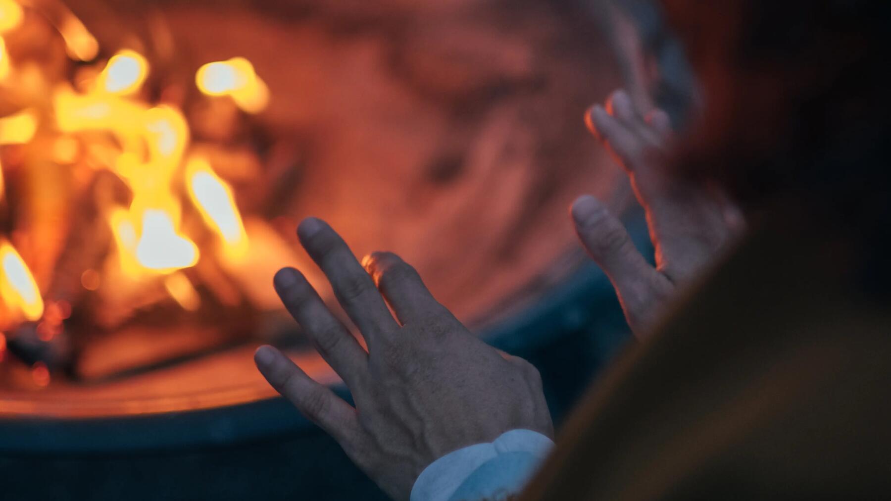 Osoba ogrzewająca ręce przy rozpalonym ognisku