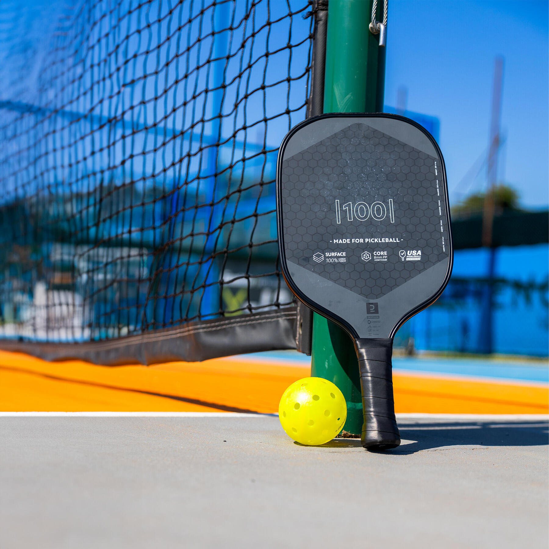 Een pickleball-racket en bal tegen een pickleball net aan op een pickleball baan.