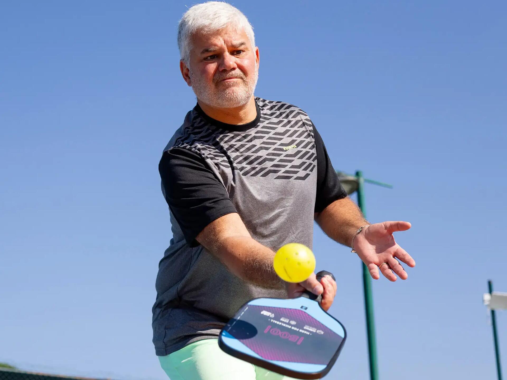 Man die pickleball speelt en de bal terug wilt slaan. 
