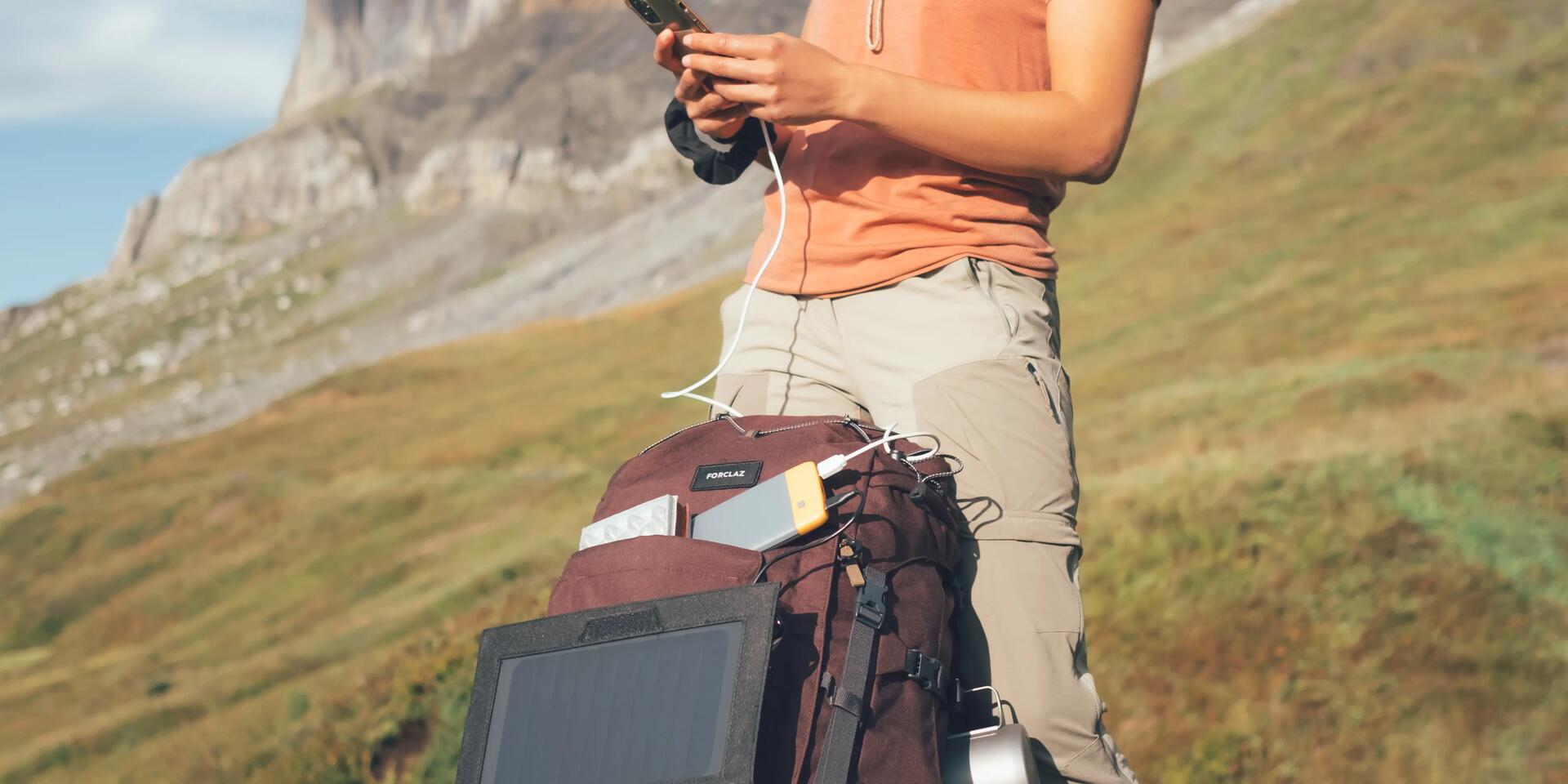 kobieta z plecakiem turystycznym w górach trzymająca telefon  podłączony do panelu słonecznego