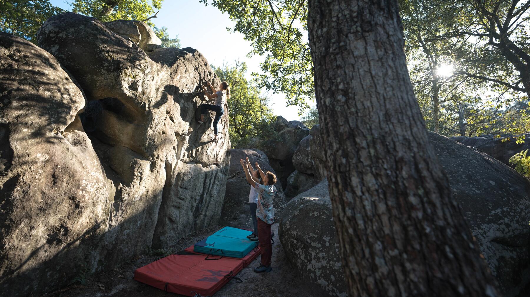 Drei Personen vor Fels am Bouldern mit Boulderpad auf dem Boden.