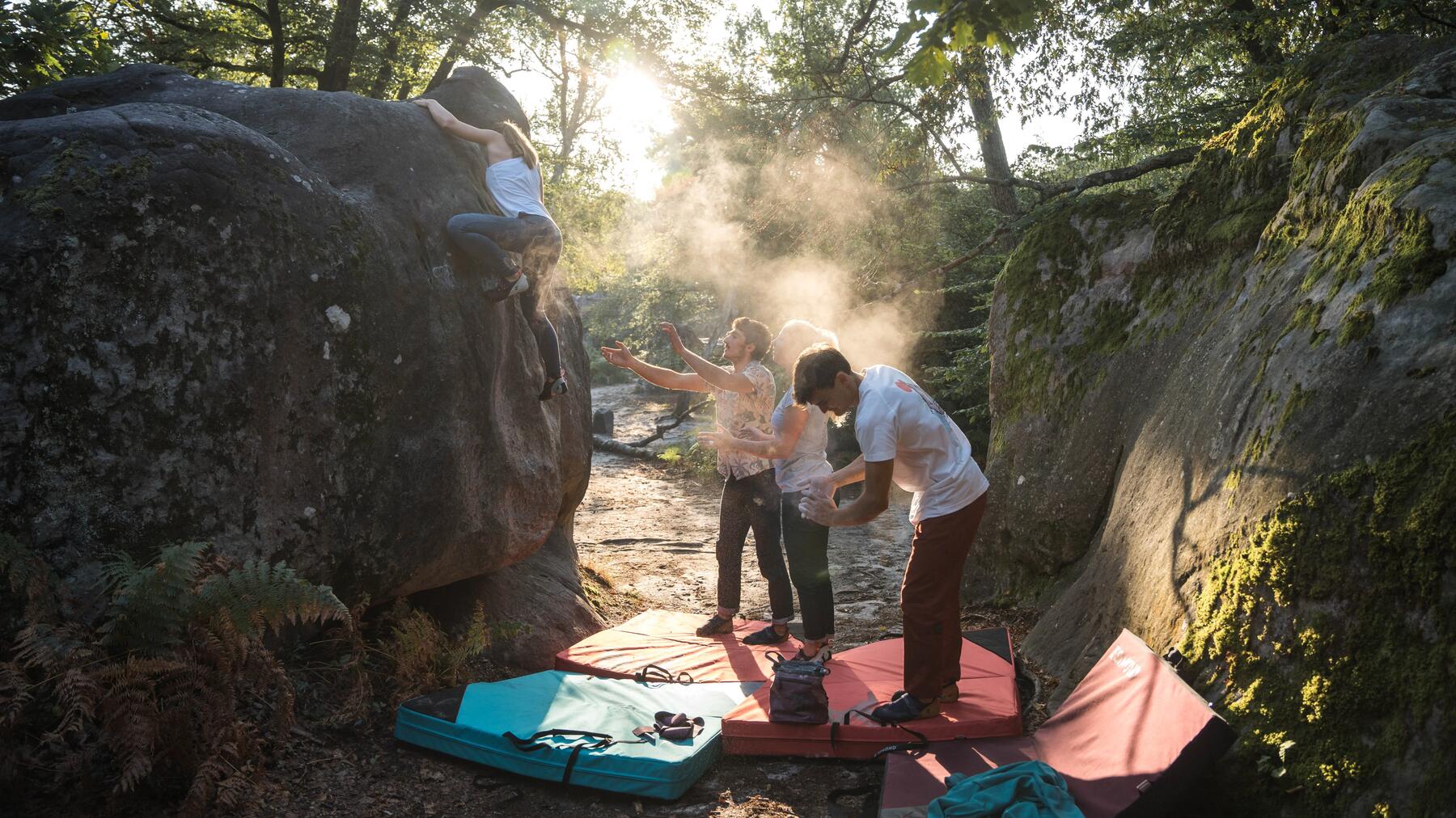 Vier Personen an Fels beim Bouldern mit Boulderpads auf dem Boden.