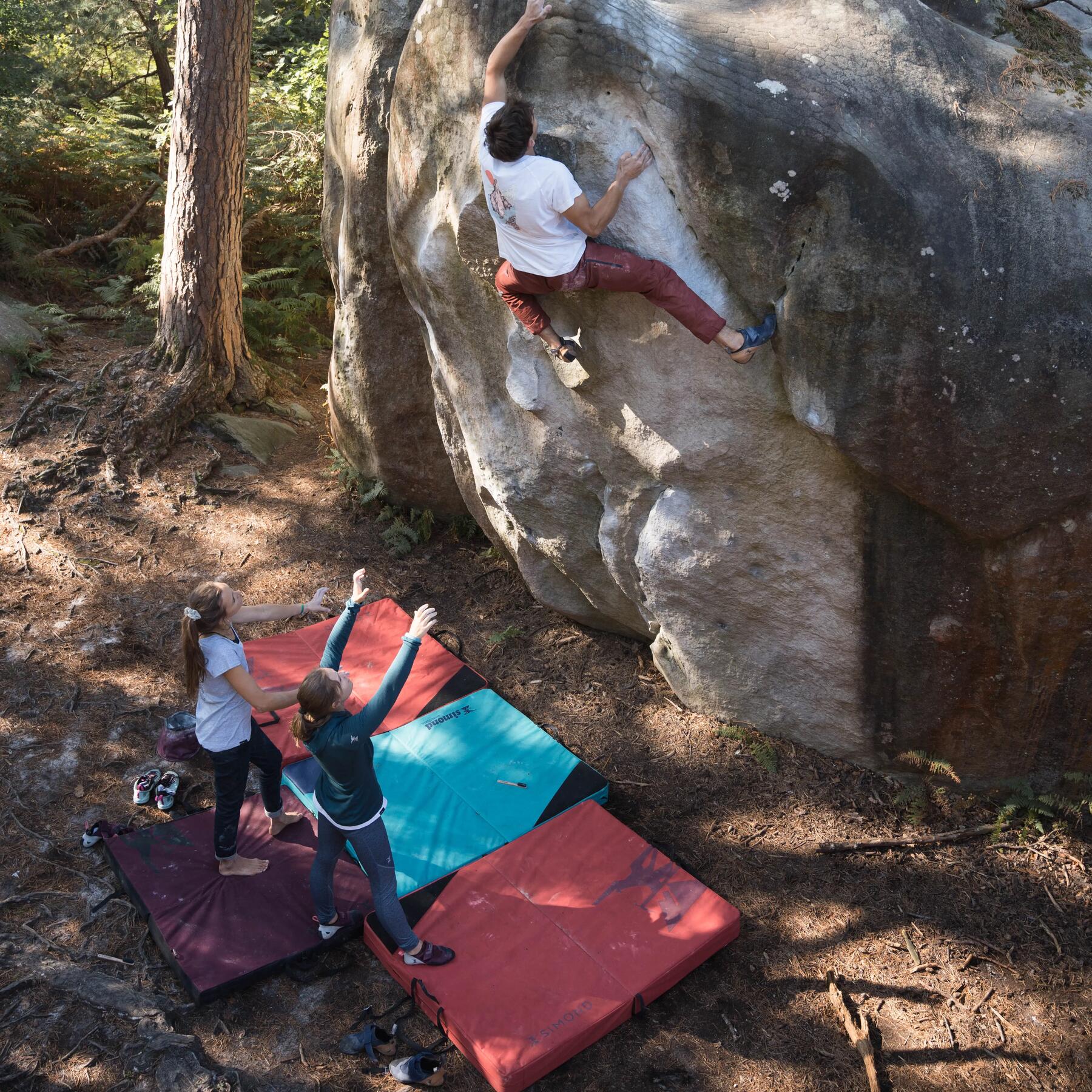 Ein Mann klettert an einem Felsen und hat ein Crashpad unter sich
