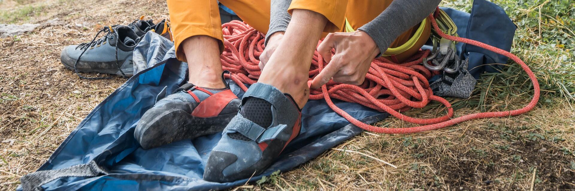 Anfänger beim Klettern, Mann zieht Kletterschuhe und Gurt an und bereitet das Seil vor