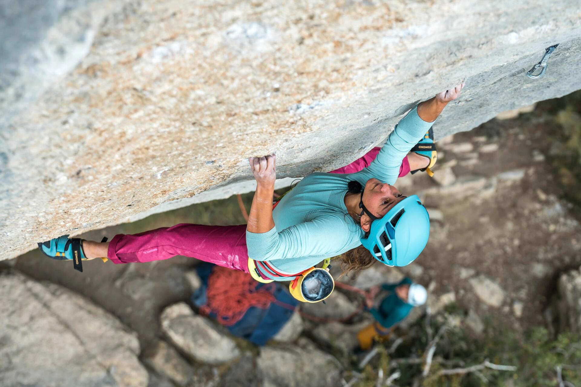 Kletterin an steiler Felswand mit langem T-Shirt und Stoffhose