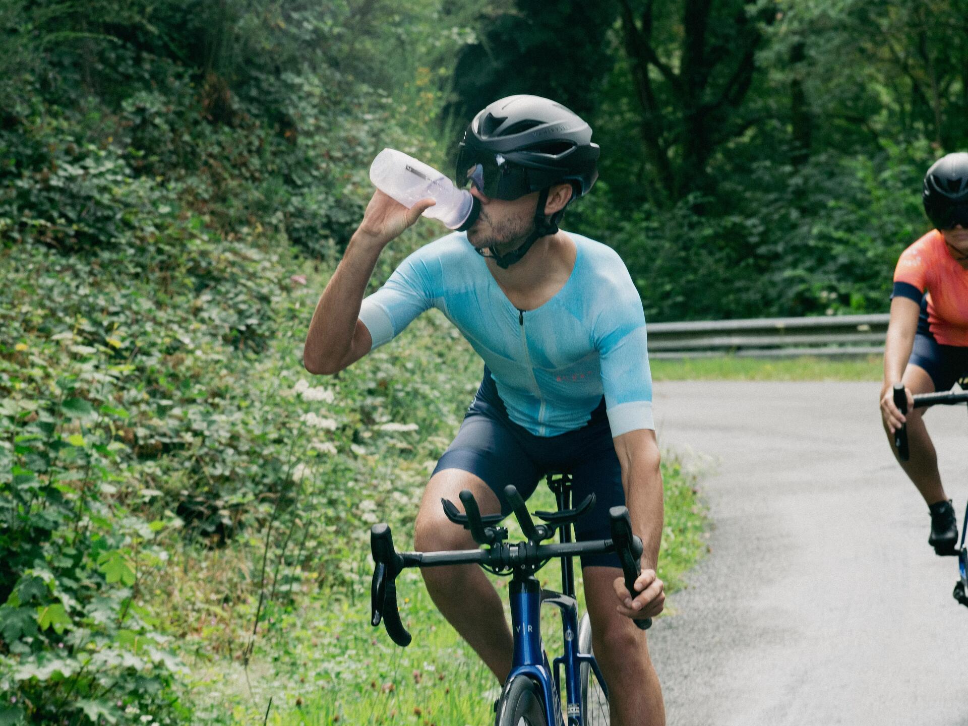 Rowerzysta w kasku i okularach rowerowych pijący izotonik z bidonu jadąc na rowerze 