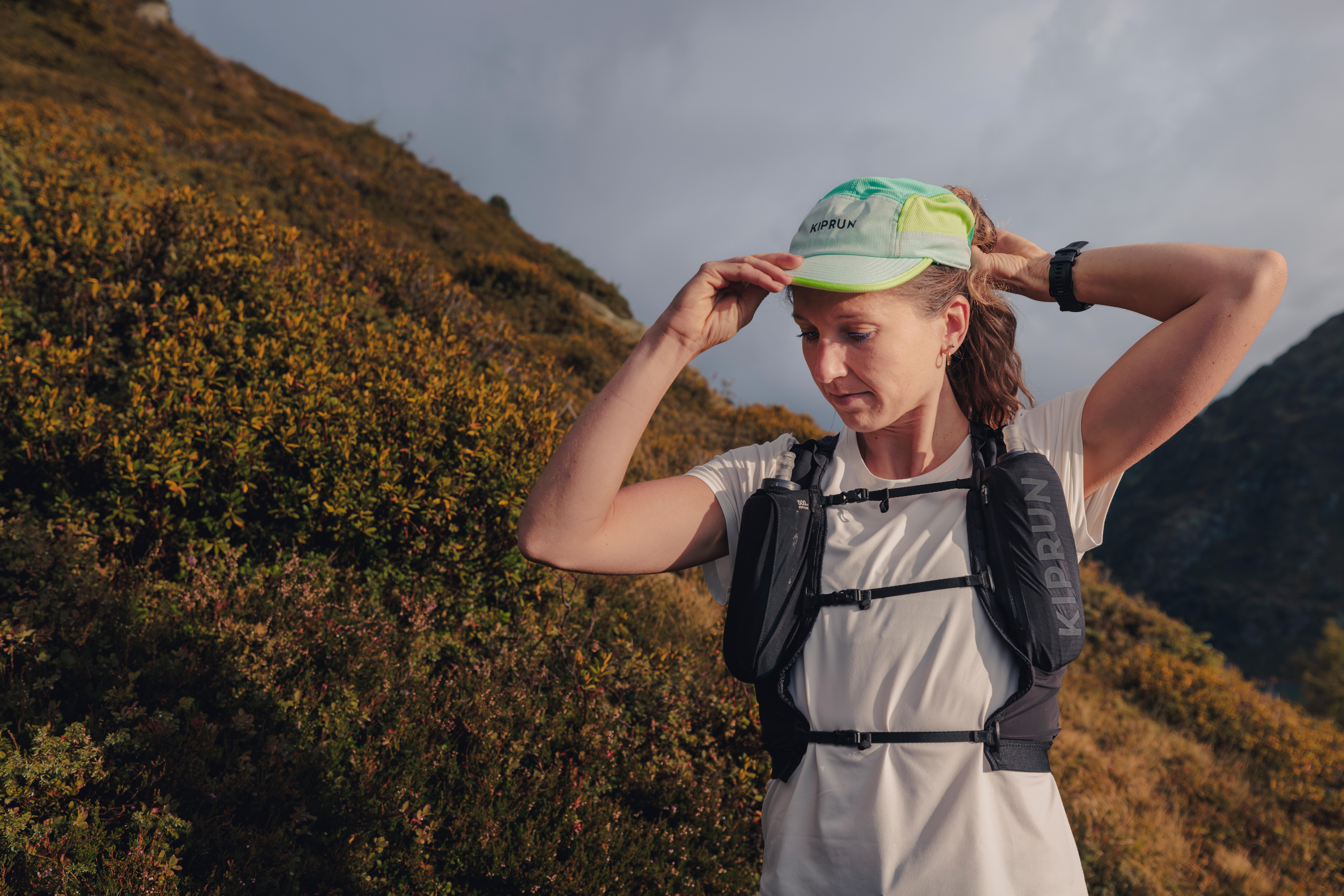 Woman wearing a black Kiprun hydration vest and running cap on a mountain trail