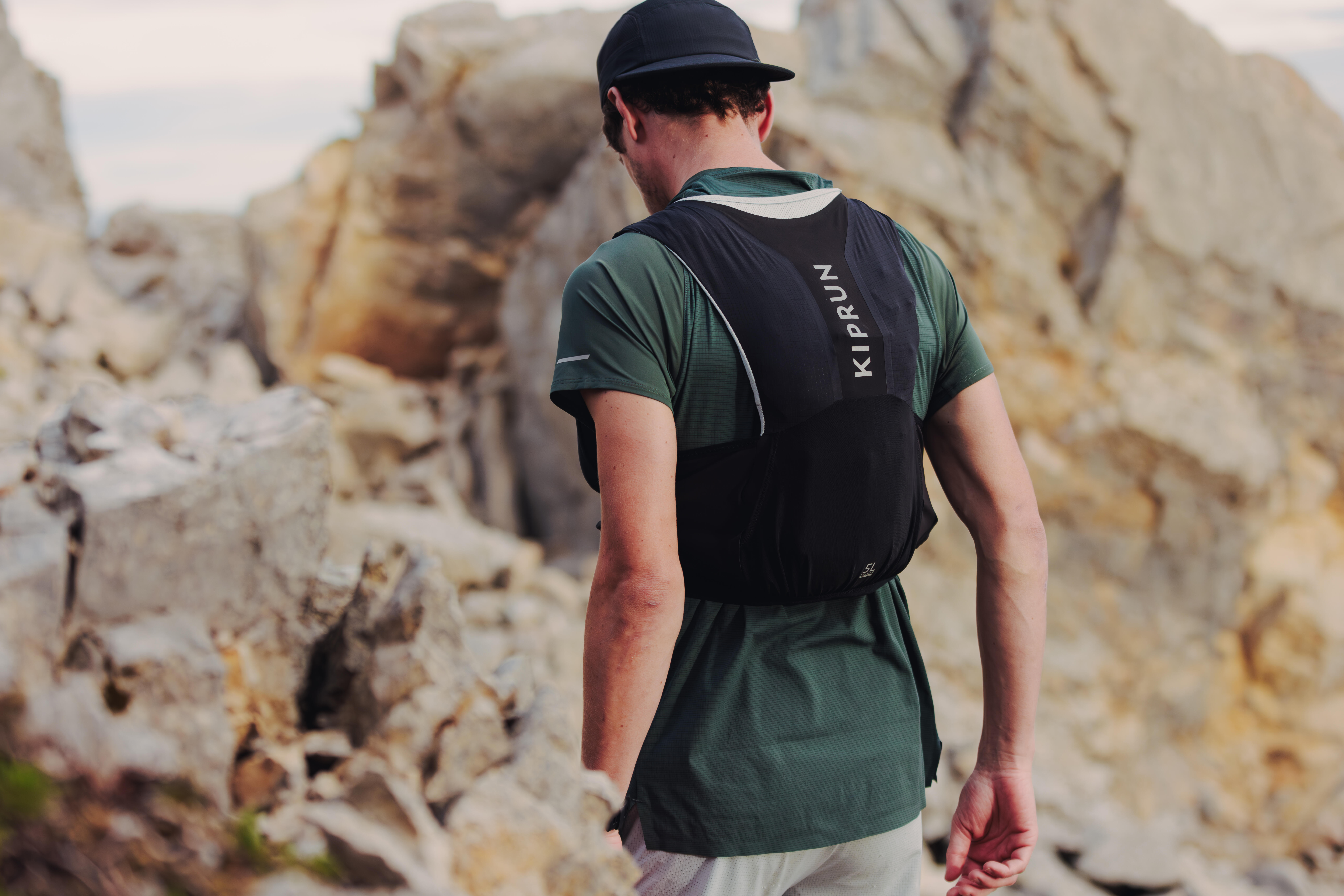 Runner wearing a black Kiprun hydration vest and running cap on a rocky mountain trail