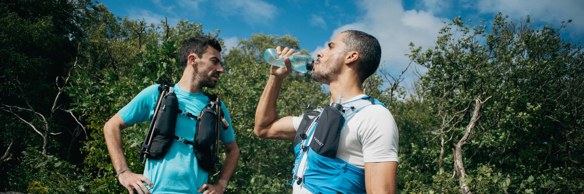 Twee mannen met hydratatievest in de natuur. Een van de twee drinkt een sportdrank.