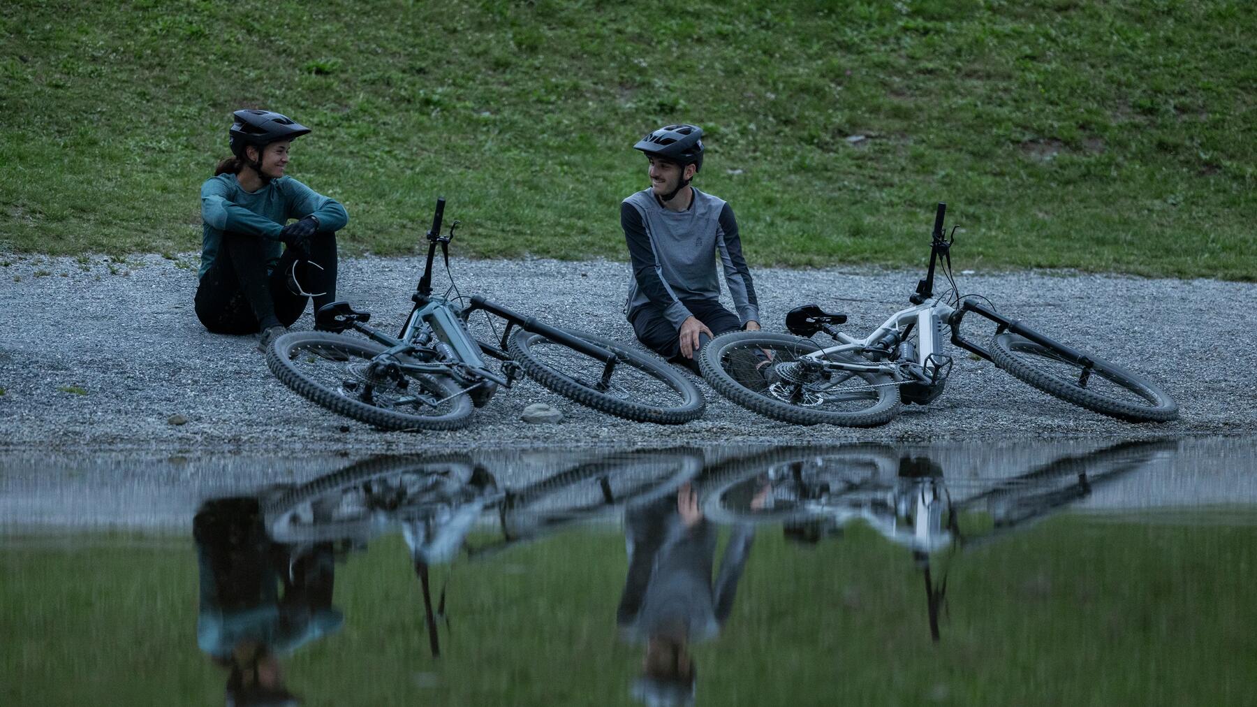 Kobieta i mężczyzna w odzieży rowerowej siedzący w plenerze obok leżących rowerów elektrycznych