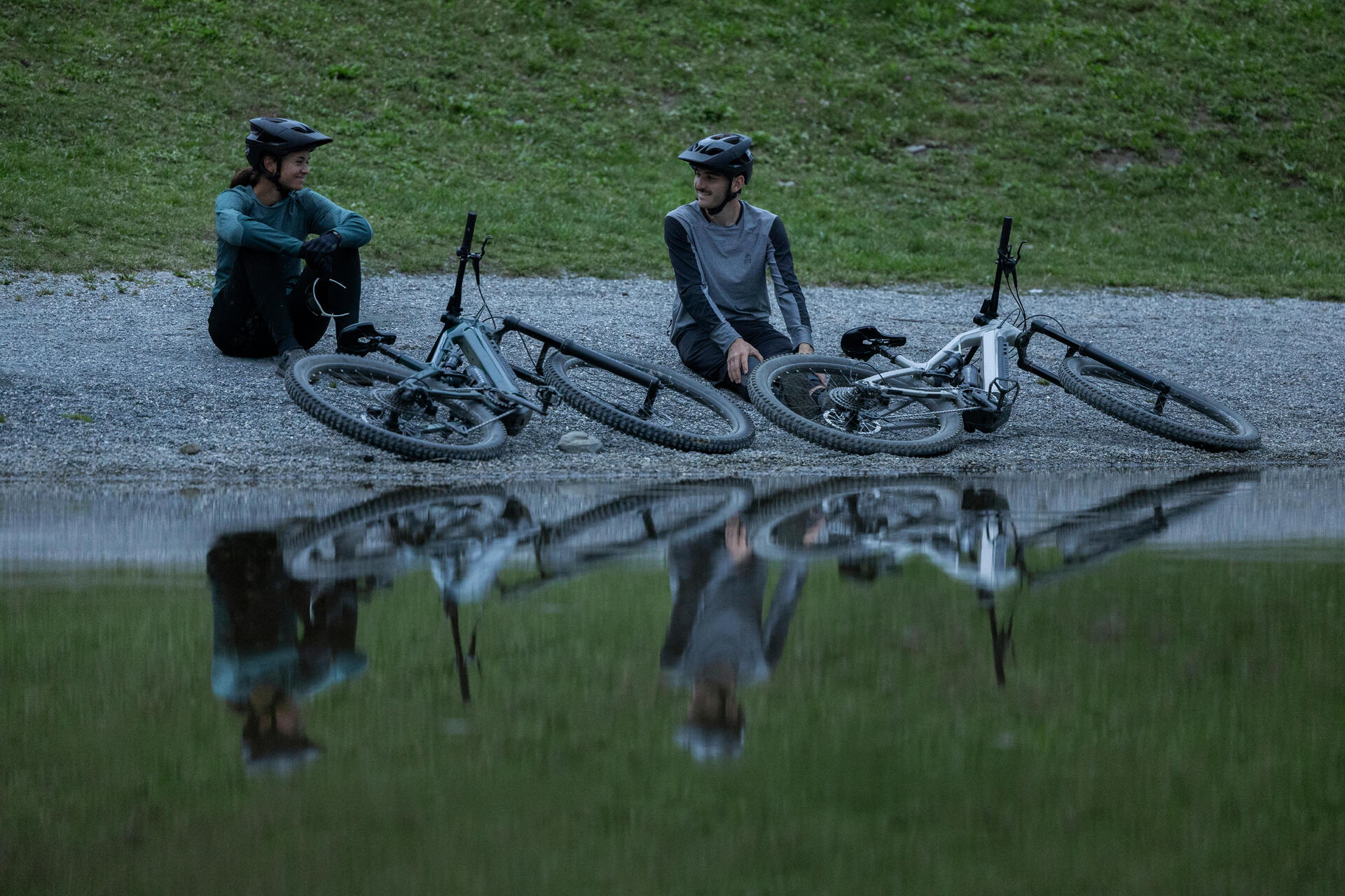 znajomi siedzący nad jeziorem z rowerami elektrycznymi