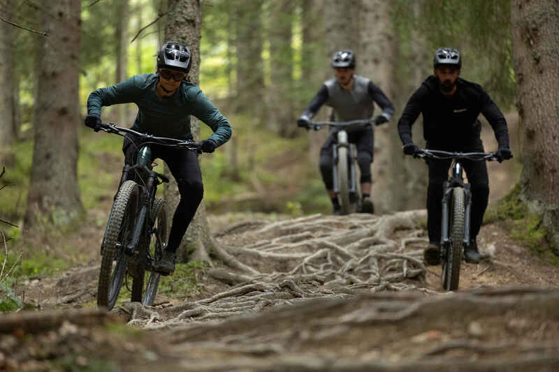 Drei Mountainbiker in voller Montur fahren durch einen Wald