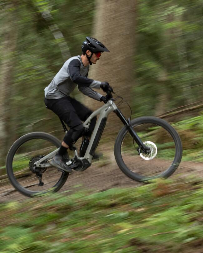 Mann mit Helm fährt mit E-Mountainbike schnell einen Anstieg im Wald hoch