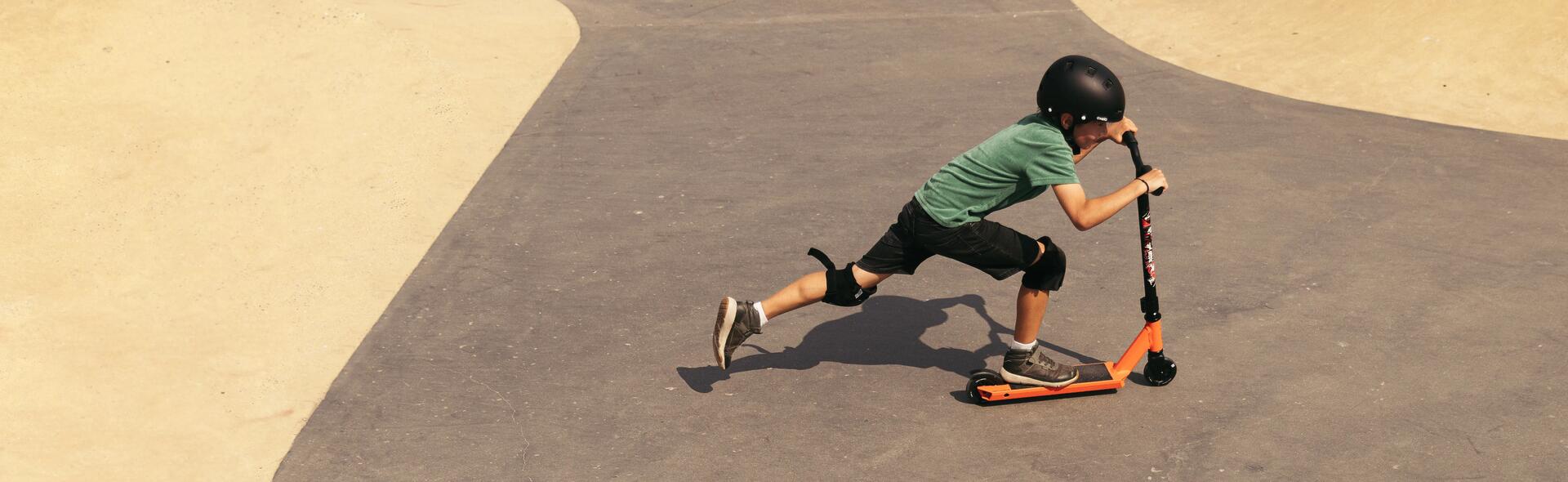 Chłopiec jeżdżący na hulajnodze wyczynowej z czarnymi kołami na skateparku