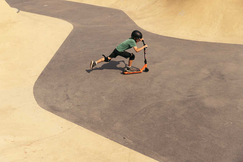Otrok s čelado vozi oranžni skiro v skejt parku.