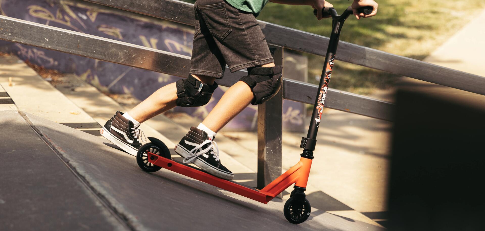 chłopiec w ochraniaczach zjeżdżający na hulajnodze na skateparku