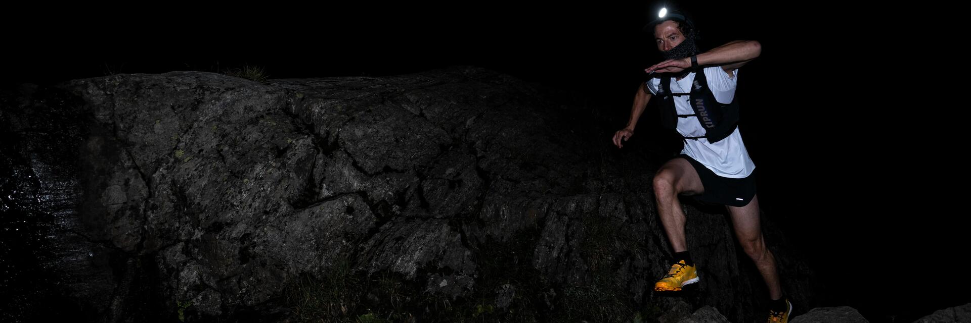 mężczyzna biegnący w nocy w kamizelce biegowej z latarką czołową na głowie