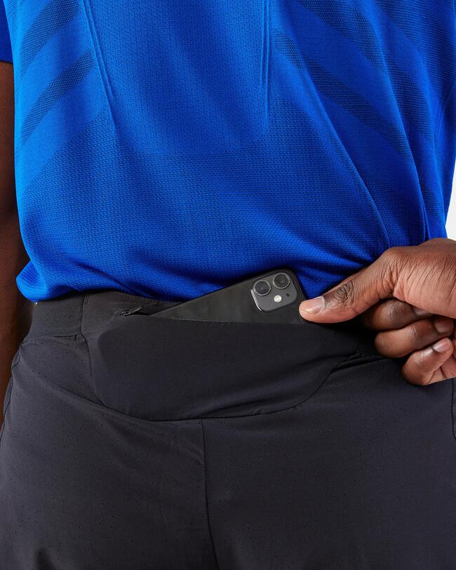 Blaue Kleidung, schwarze Hose, Hand steckt schwarzes Smartphone  in Gesäßtasche.
