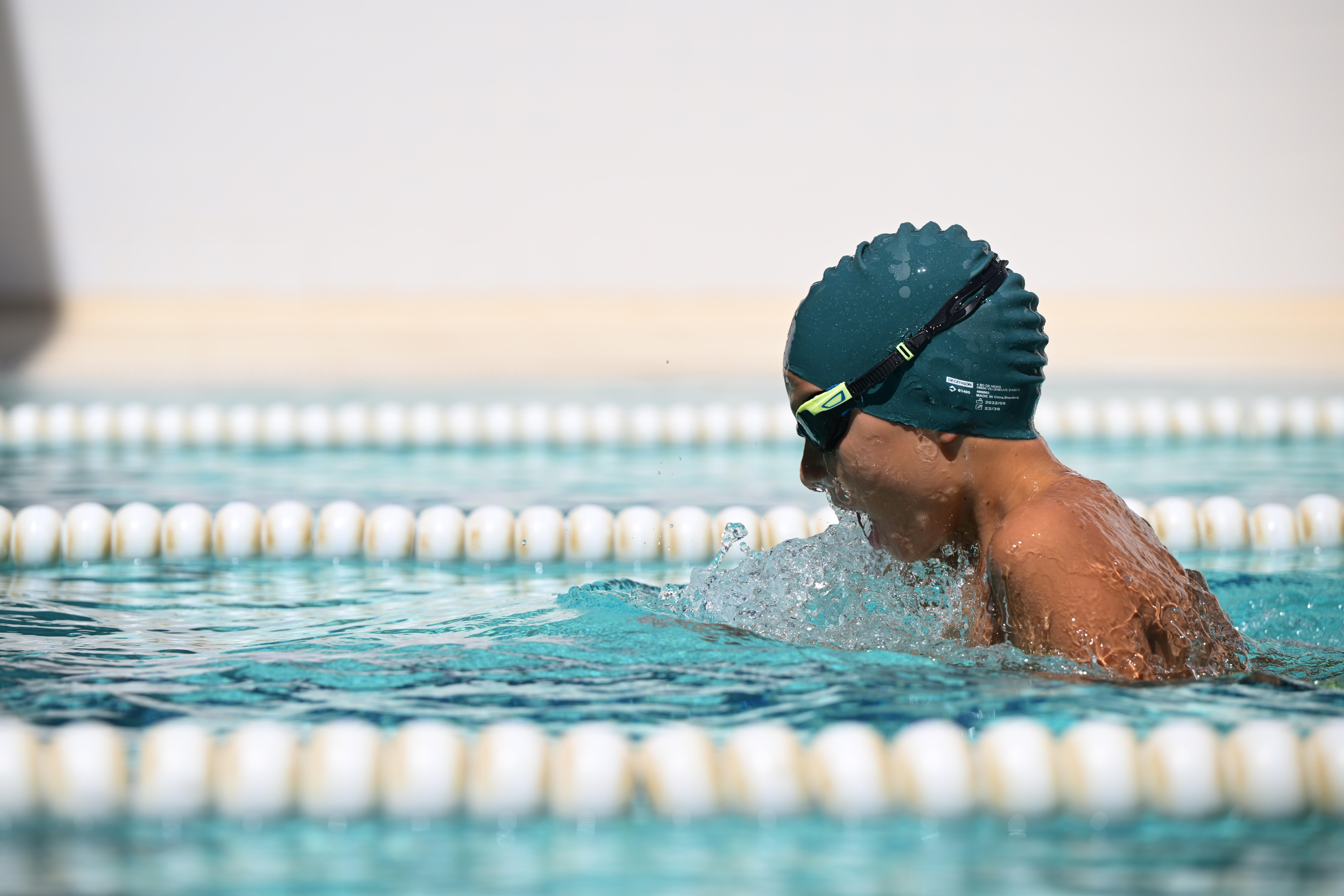 Swimmer wearing a dark green swim cap and goggles in a swimming pool.