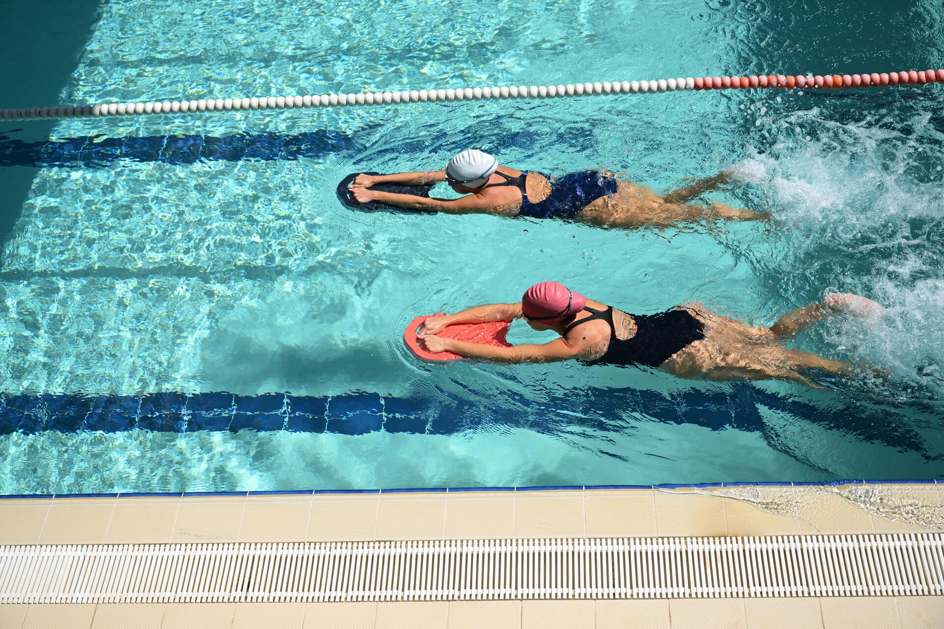 Dwie kobiety uczące się pływać z deską do pływania