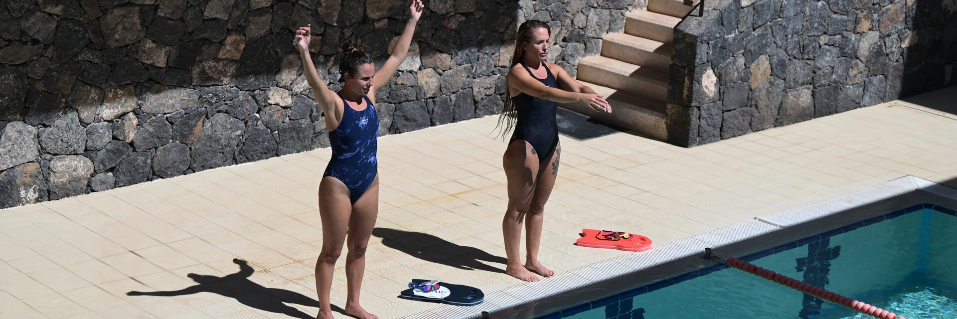 Zwei Frauen tragen Outdoor-Schwimmanzüge und stehen am Beckenrand