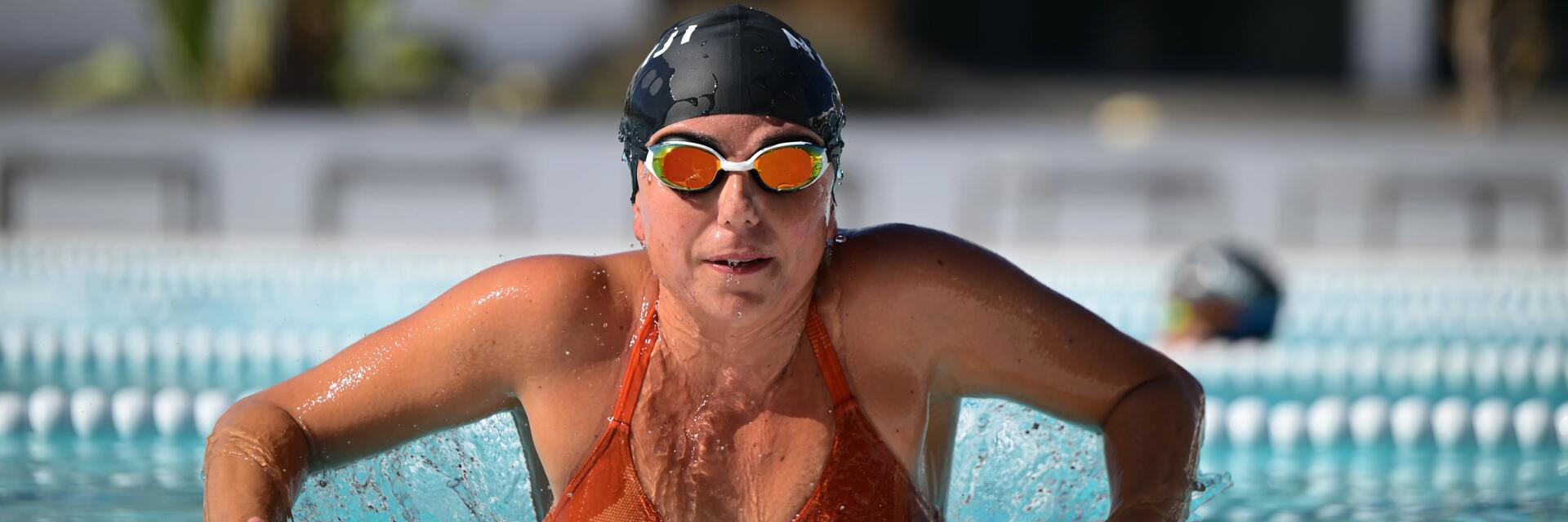 Kobieta w czepku i okularkach pływackich opierająca sie o brzeg basenu sportowego