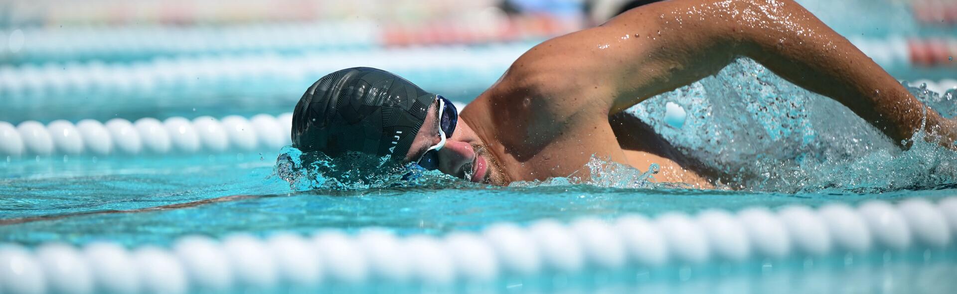 mężczyzna w czepku kąpielowym i okularach pływackich wykonujący trening szybkościowy