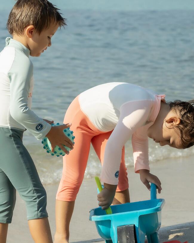 Zwei Kinder spielen am Strand im Sand, UV-Anzüge, Wasserball