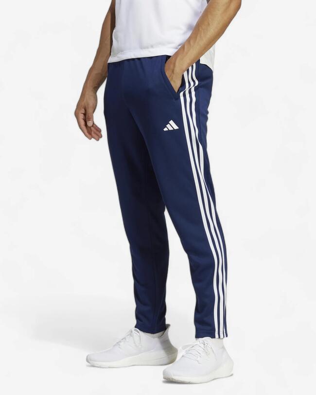 Mann in dunkelblauer Adidas Trainingshose mit weißen Streifen und weißem T-Shirt, seitliche Ansicht.