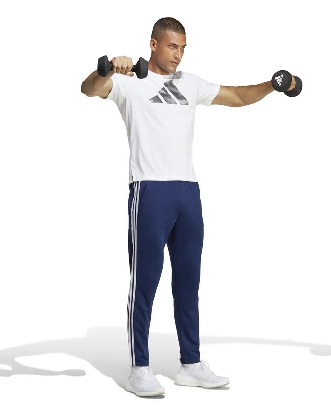 Mann macht Seitheben mit Kurzhanteln in weißem T-Shirt und blauer Adidas-Trainingshose.