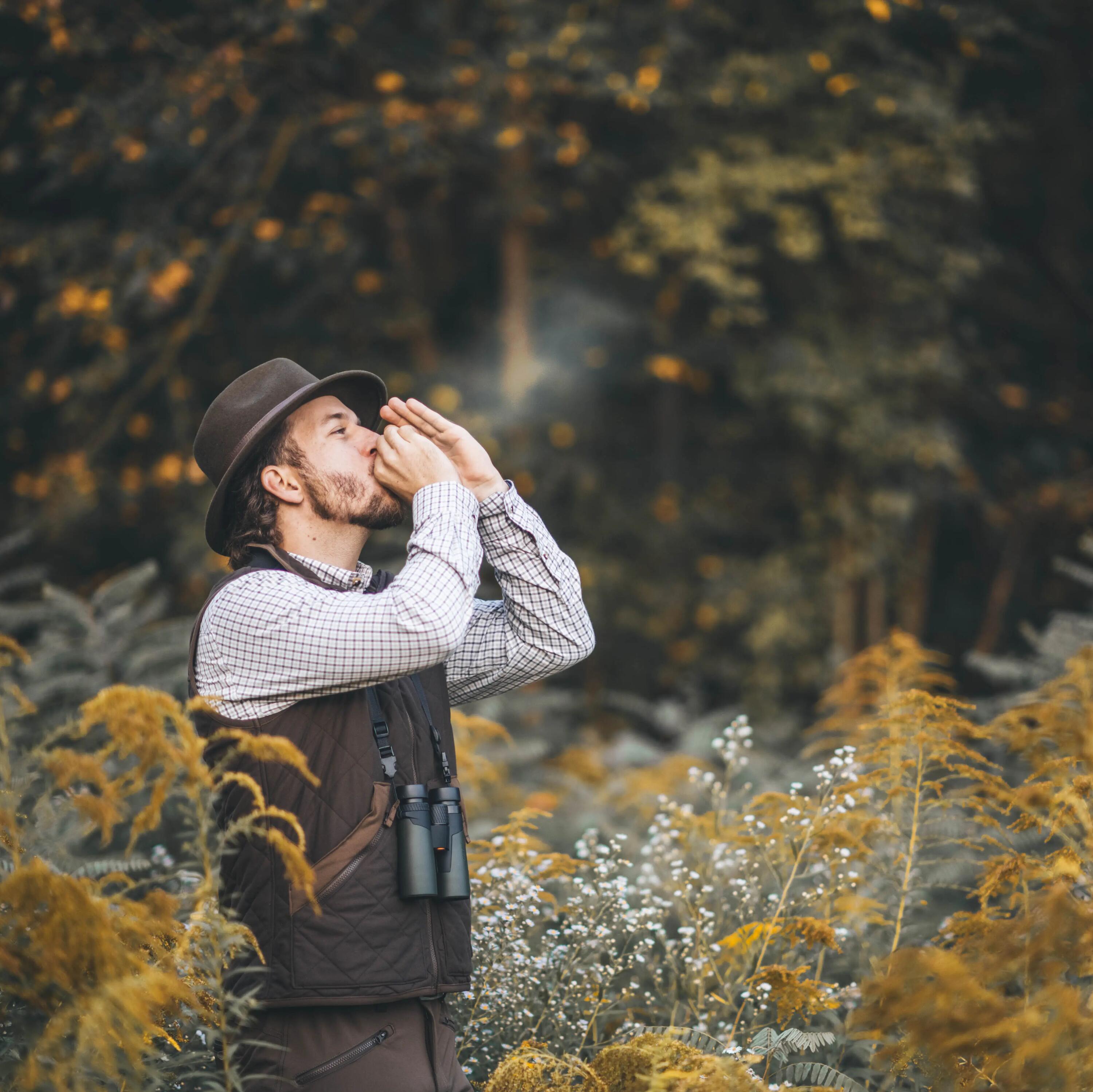 Ein Mann in Jagdbekleidung steht im Wald und haucht in die Luft