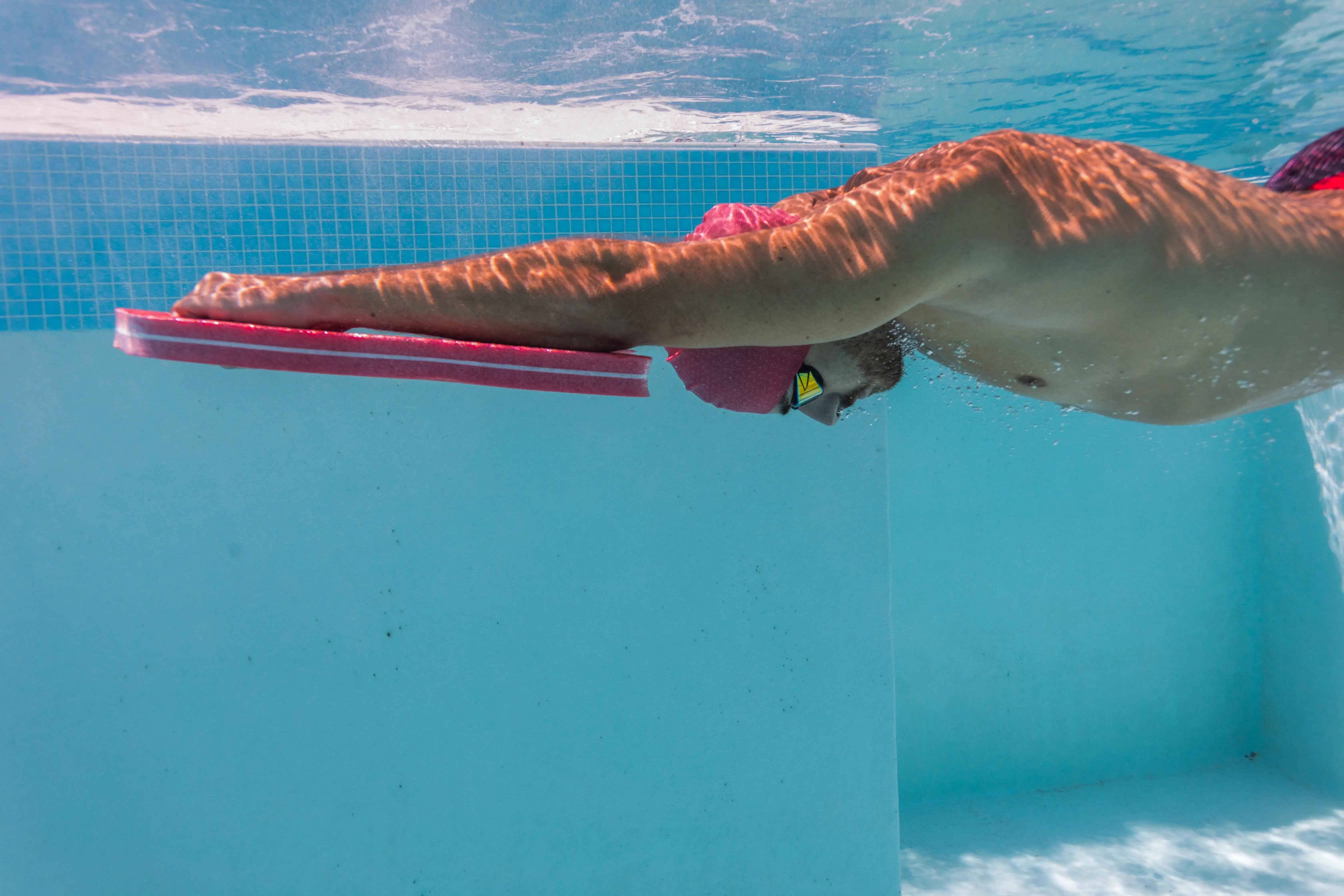 Swimmer using a pink kickboard underwater in a swimming pool.