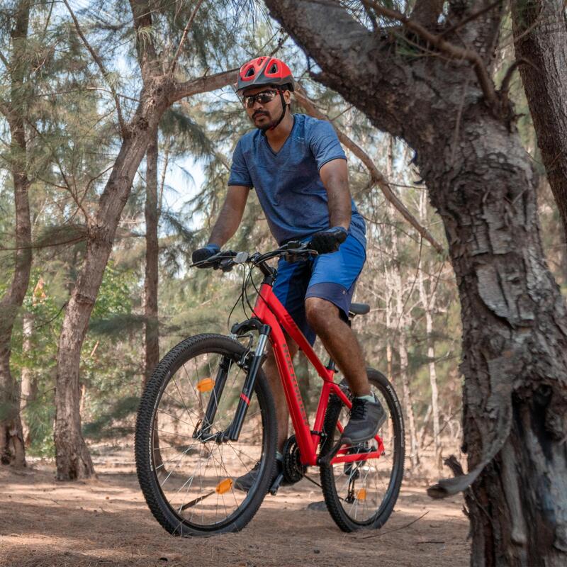 Moški vozi rdeče gorsko kolo skozi gozd s čelado in zaščitno opremo.