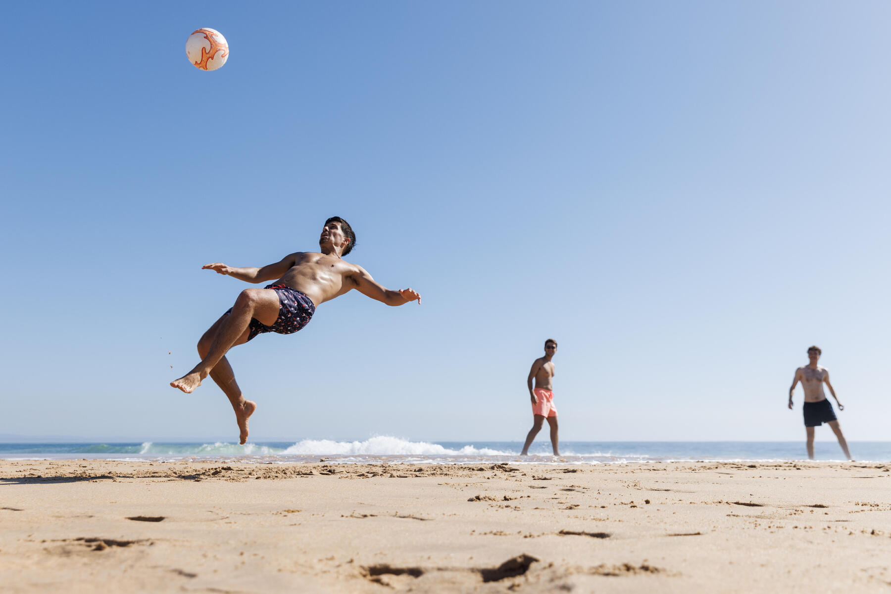 Mężczyźni w strojach sportowych grający w piłkę nożną na plaży