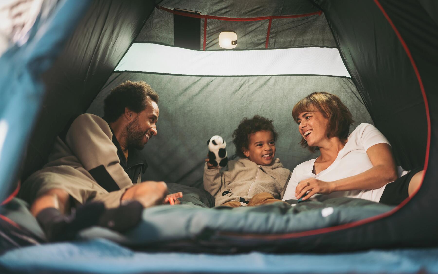A family of three relaxing inside a tent smiling